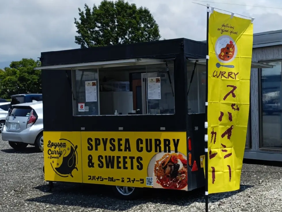 黒と黄色の車体に SPYSEA CURRY & SWEETS と書かれたキッチンカーと、スパイシーカレーののぼり